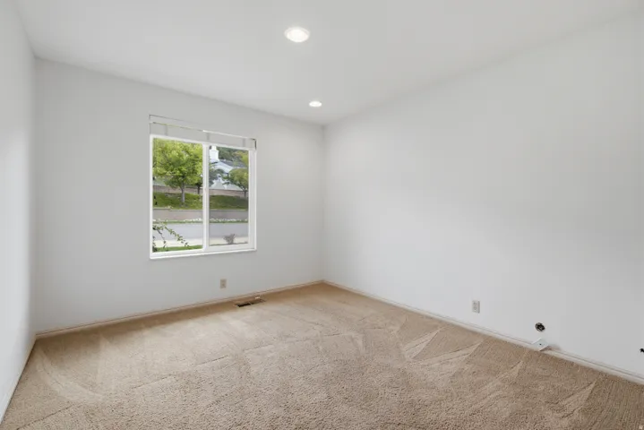 Recessed ceiling lights illuminate this room featuring wall-to-wall carpeting and a large window