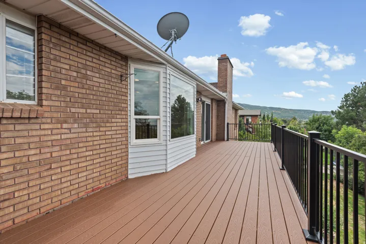 Expansive outdoor deck with wood-finish decking, black metal railing, and a brick exterior