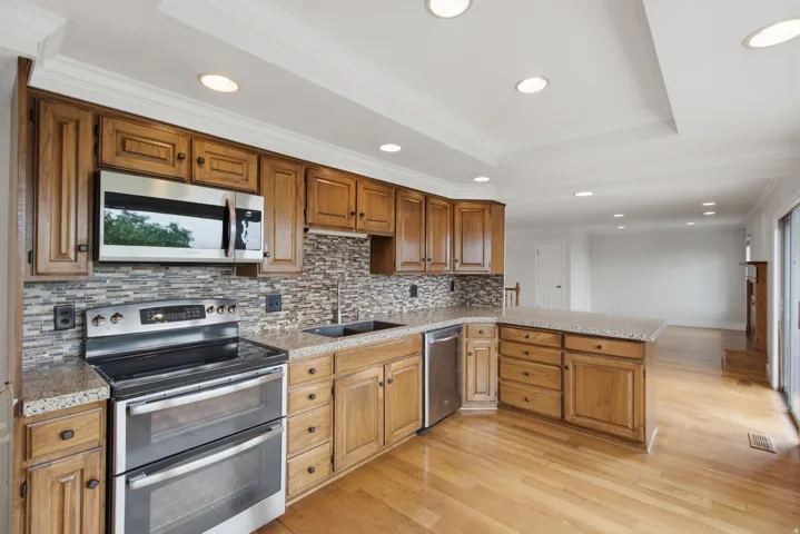 Kitchen featuring wood cabinetry, stainless steel appliances, a mosaic tile backsplash, and light-toned countertops