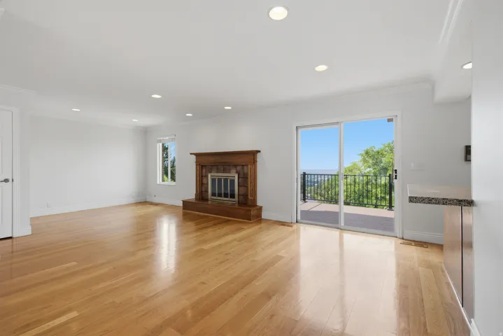 Hardwood flooring, a wood-surround fireplace with a hearth, recessed lighting, and a sliding glass door leading to an outdoor deck with metal railings