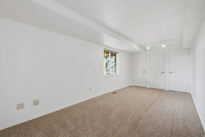 Carpeted room with white walls, multiple white panel doors, and track lighting