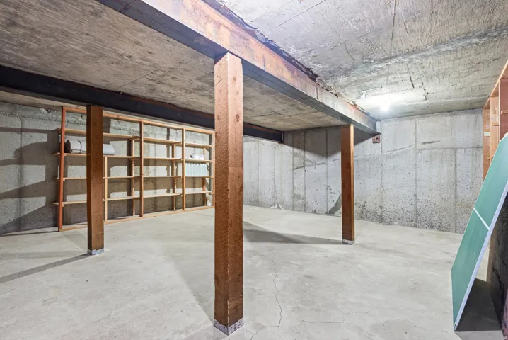 Concrete floor and walls, exposed wooden support beams, and built-in wooden shelving