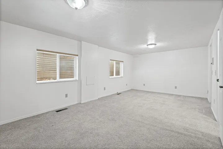 Spacious interior with neutral carpeting, white walls, and two windows with blinds, complemented by two flush-mount ceiling lights