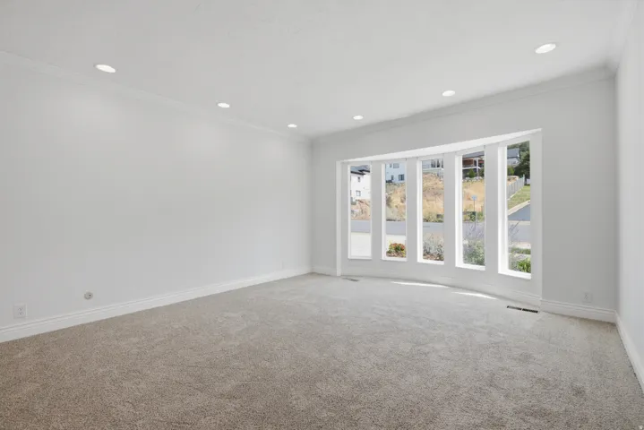 Recessed lighting, crown molding, and a curved bay window complement the neutral-toned walls and carpeting