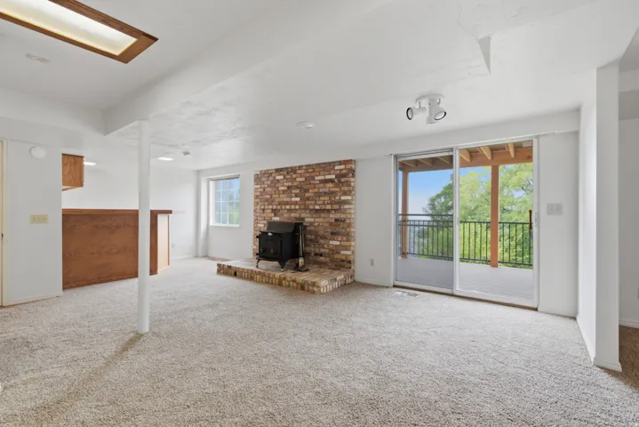 Expansive carpeted area with a brick-faced wood-burning stove and hearth, complete with a built-in wet bar featuring wood cabinetry