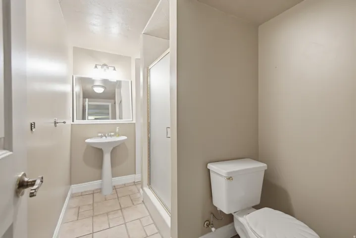 Pedestal sink with a vanity mirror, tile flooring, and a shower enclosure