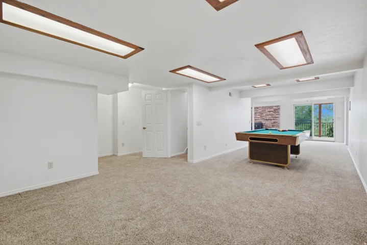 Spacious room with plush carpet flooring, recessed lighting with wood-finish trim, and a sliding glass door leading to an outdoor area
