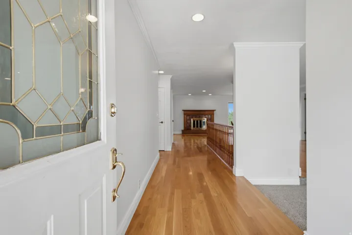 Entryway featuring a decorative glass door, brass hardware, wood-finish flooring, recessed lighting, and a wood-paneled fireplace in the background