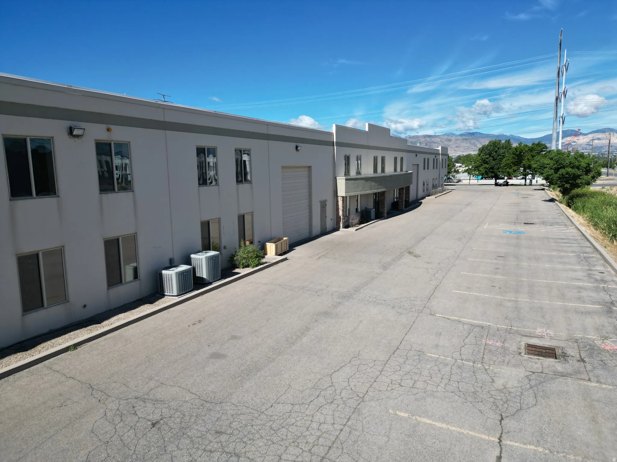 Expansive paved parking area, two-story commercial building, multiple windows, large garage door, and visible HVAC units