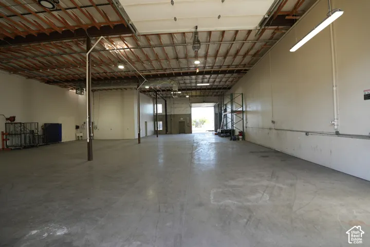 Concrete flooring, exposed wood beam ceiling, white interior walls, overhead fluorescent lighting, roll-up door
