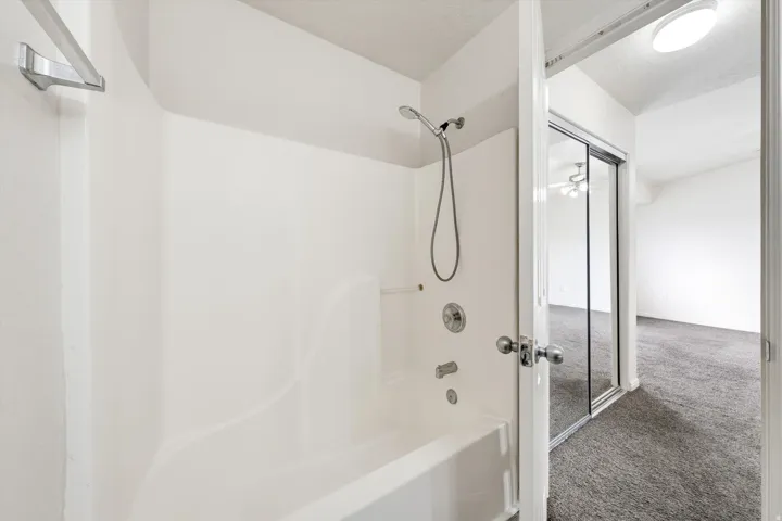 Bathtub with an integrated shower, chrome fixtures, and a showerhead with an attached hose