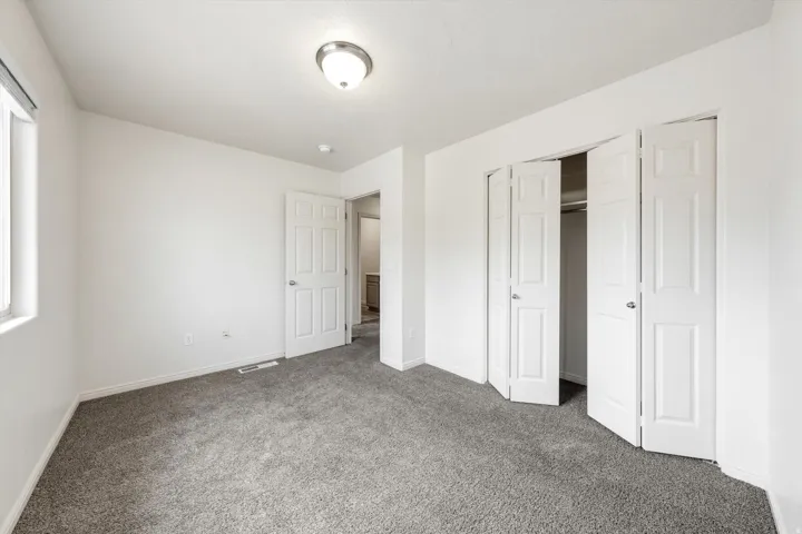 White interior walls with gray carpeting, featuring a window with white trim, a flush mount ceiling light fixture, and bifold closet doors