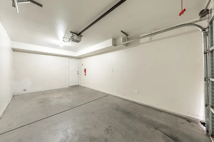Single-vehicle garage with a concrete floor, an overhead automatic garage door opener, and a side access door