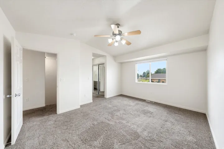 Carpeted room featuring a ceiling fan with light fixture, white walls, and a window