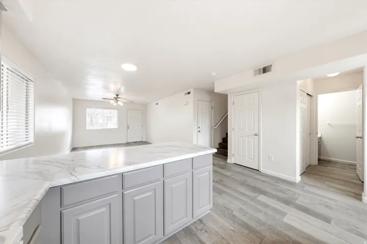 Kitchen island with light gray cabinetry and a light-toned countertop, wood-finish flooring, white walls, and a ceiling fan