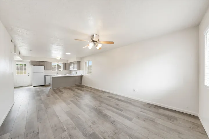 Open-concept living area with wood-finish flooring, a ceiling fan, and a kitchen featuring grey cabinetry, white countertops, and white appliances