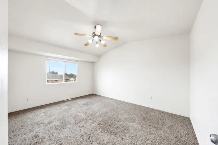 Vaulted ceiling room featuring a ceiling fan with light kit, a large window, and wall-to-wall carpeting