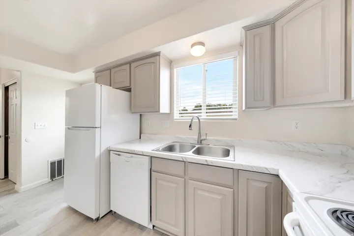 Kitchen featuring light wood-finish flooring, white appliances, dual basin stainless steel sink, and light-toned cabinetry with white countertops