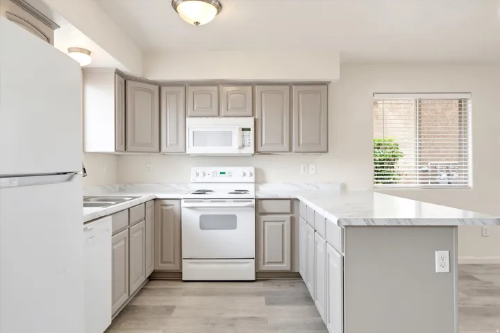 Kitchen featuring light gray cabinetry, white appliances, marble-look countertops, and wood-finish flooring