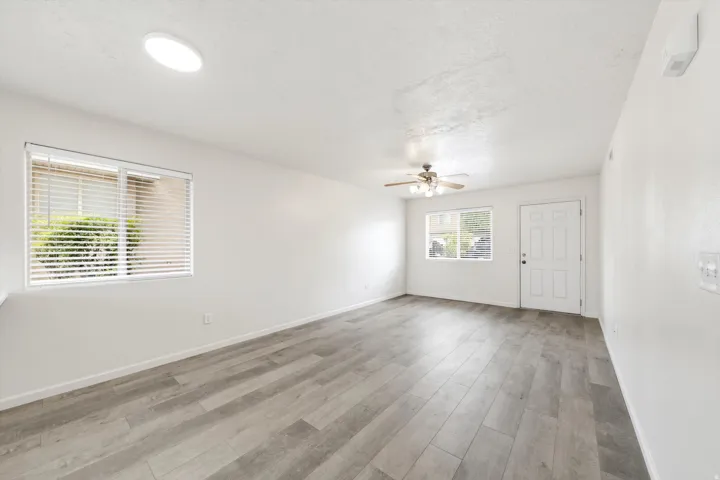 Spacious room with wood-finish flooring, white walls, and multiple windows with blinds