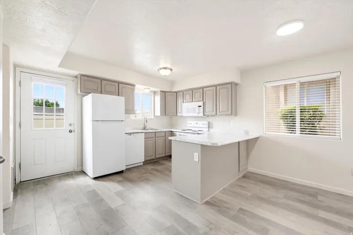 Kitchen featuring gray cabinetry, light countertops, wood-finish flooring, and white appliances