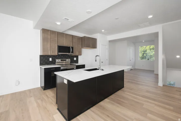Modern kitchen featuring custom cabinetry in warm wood tones and black, quartz countertops, stainless steel appliances, and a large waterfall-edge island with seating
