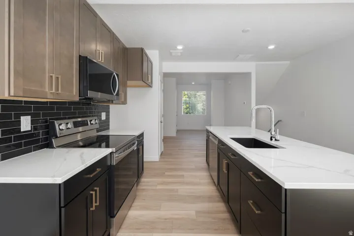 Modern kitchen featuring a large central island with an undermount sink, stainless steel appliances, wood-finish flooring, white countertops, and a black subway tile backsplash