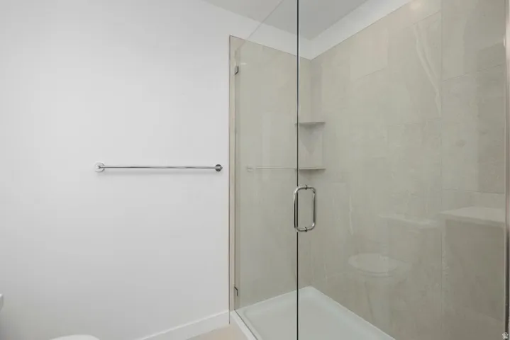 Glass-enclosed shower with a chrome handle, tiled interior walls, integrated shelving, and a white shower pan