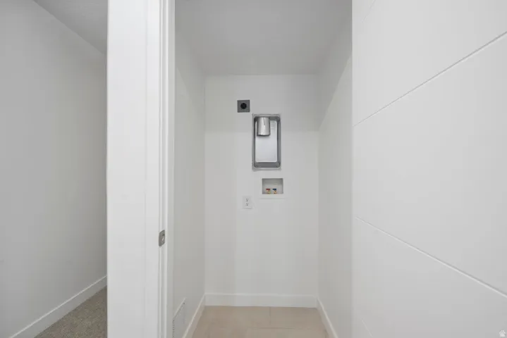 Dedicated laundry area featuring tile flooring, white walls, and a shiplap accent wall