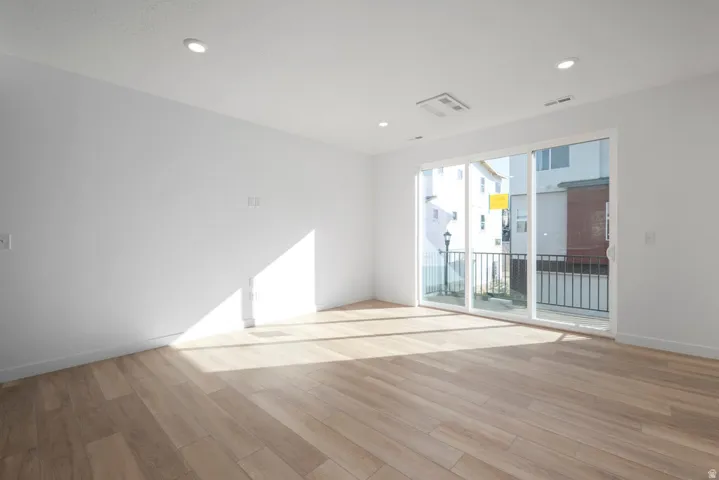 Bright, open living space featuring gleaming wood-finish flooring, recessed ceiling lighting, and expansive glass doors opening to a private balcony with metal railings