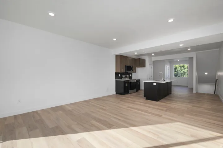 Open-concept living space featuring wood-finish flooring, recessed lighting, and a kitchen island with an integrated sink