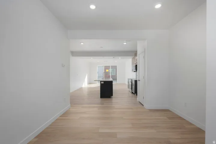Recessed lighting, wood-finish flooring, white walls, kitchen island with sink, and stainless steel appliances