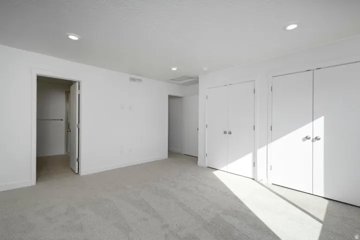 Recessed lighting illuminates neutral carpeting and white walls