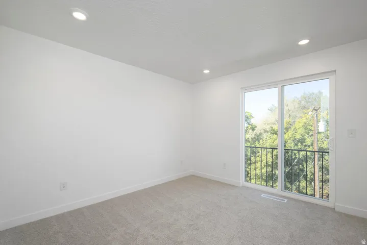 Recessed lighting, light gray carpet flooring, white walls, and a sliding glass door opening to an exterior balcony with black metal railing