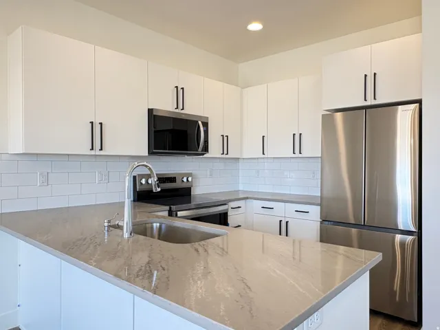 Modern kitchen featuring white cabinetry, stainless steel appliances, a subway tile backsplash, a stainless steel sink with a chrome faucet, and substantial counter space