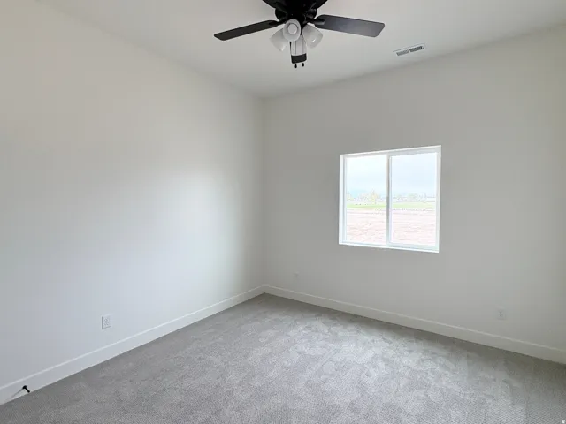 Neutral wall paint with gray carpeting, ceiling fan with integrated lighting, and a single window