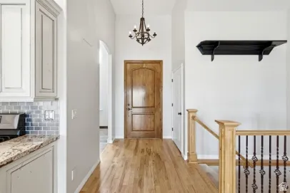 Hardwood flooring, wood entry door, wrought iron chandelier, wood railing with wrought iron balusters, and granite countertops