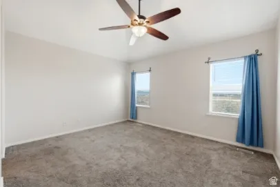 Spacious room featuring neutral carpeting, two windows, and a ceiling fan with integrated lighting