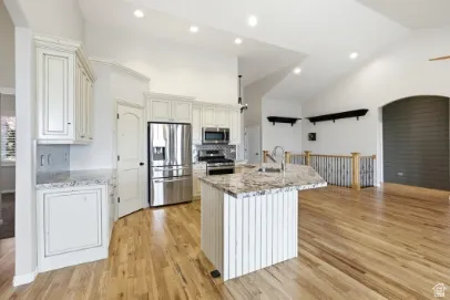 Vaulted ceilings with recessed lighting, stainless steel appliances, wood-finish flooring, granite countertops, and white cabinetry