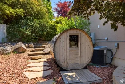 Barrel sauna with a wood-plank entry, set amidst a landscaped area with natural stone steps and mature plantings