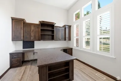Integrated built-in cabinetry and desk with stone-finish countertops, wood-finish flooring, and high vaulted ceilings