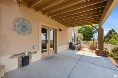 Covered concrete patio with exposed beam ceiling, double glass doors, stucco exterior, and privacy fencing