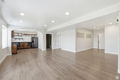 Spacious open-concept room with wood-finish flooring, recessed lighting, and an archway leading to a built-in wet bar featuring dark wood cabinetry and open shelving