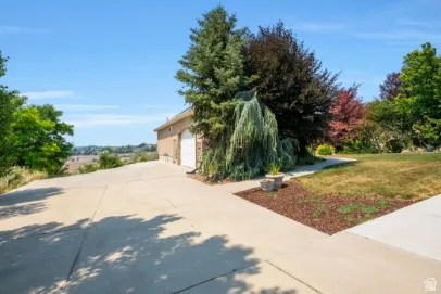 Attached two-car garage with white paneled doors, expansive concrete driveway, and established perennial landscaping
