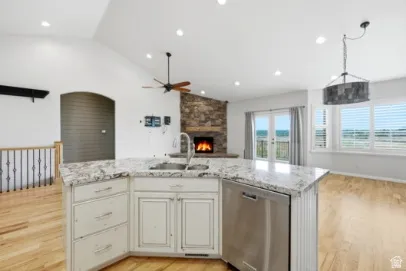 Kitchen island with a built-in sink and stainless steel dishwasher, stone-clad fireplace, vaulted ceilings, and wood-finish flooring
