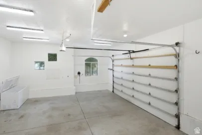 Spacious garage with concrete flooring, multiple fluorescent ceiling lights, a garage door, and an arched window