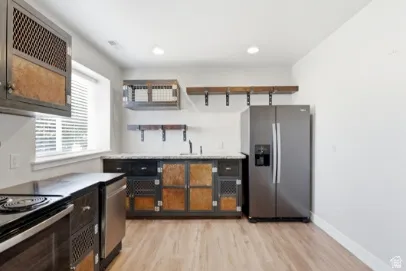 Kitchen featuring wood-finish flooring, stainless steel refrigerator, dark cabinetry with metal detailing, built-in shelving, and a window with blinds