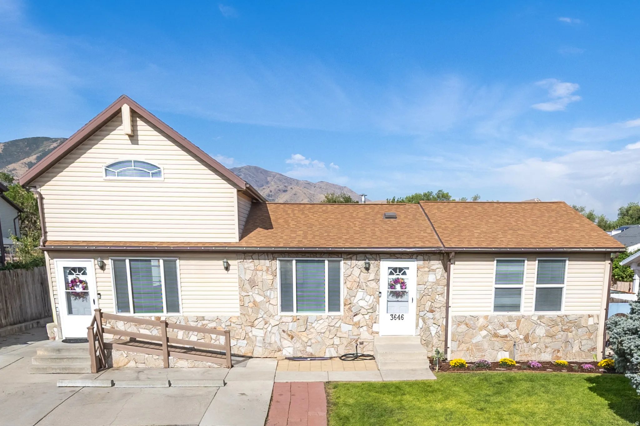 Exterior featuring stone facade detailing, light-toned siding, a brown shingle roof, a front lawn, and a ramp access