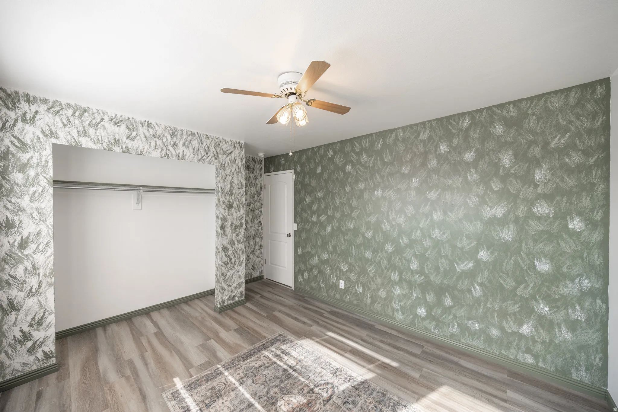 Wood-finish flooring, ceiling fan with integrated lighting, open closet with hanging rod, and a solid interior door