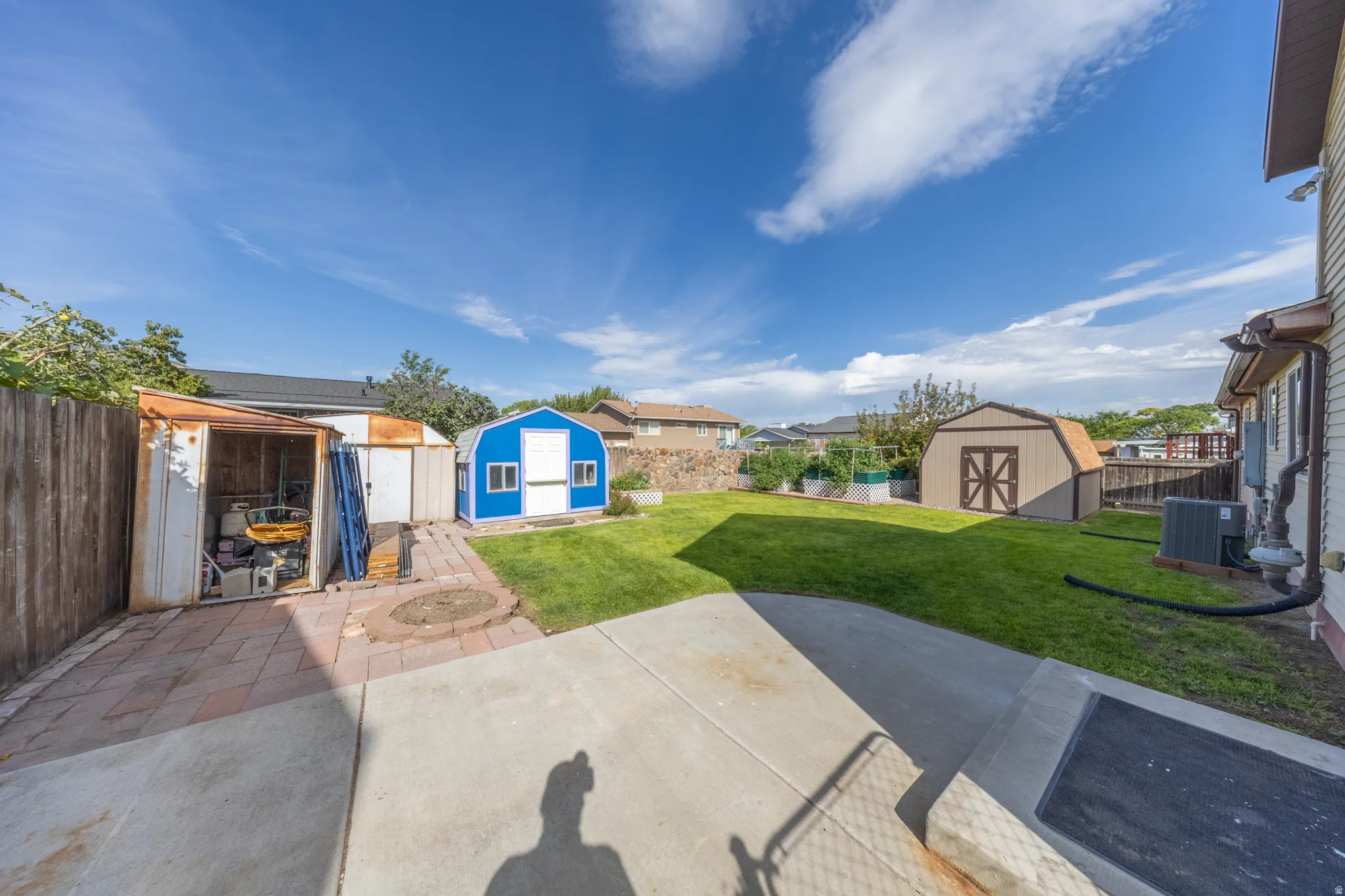 Expansive backyard featuring a concrete patio, a manicured lawn, and multiple storage sheds
